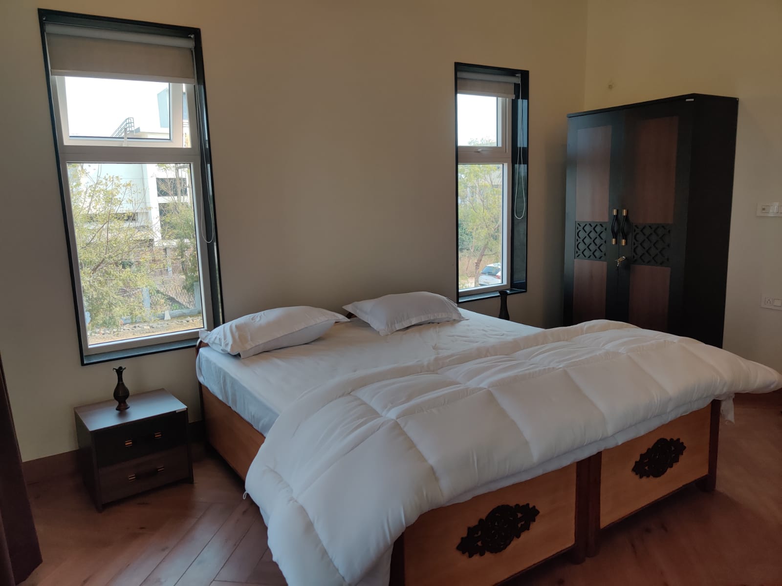 Sunlit bedroom with twin windows and wooden wardrobe
